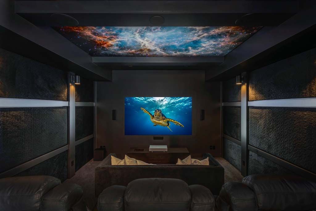 Home theater with a galaxy ceiling, large screen, black seating, and underwater film playing.