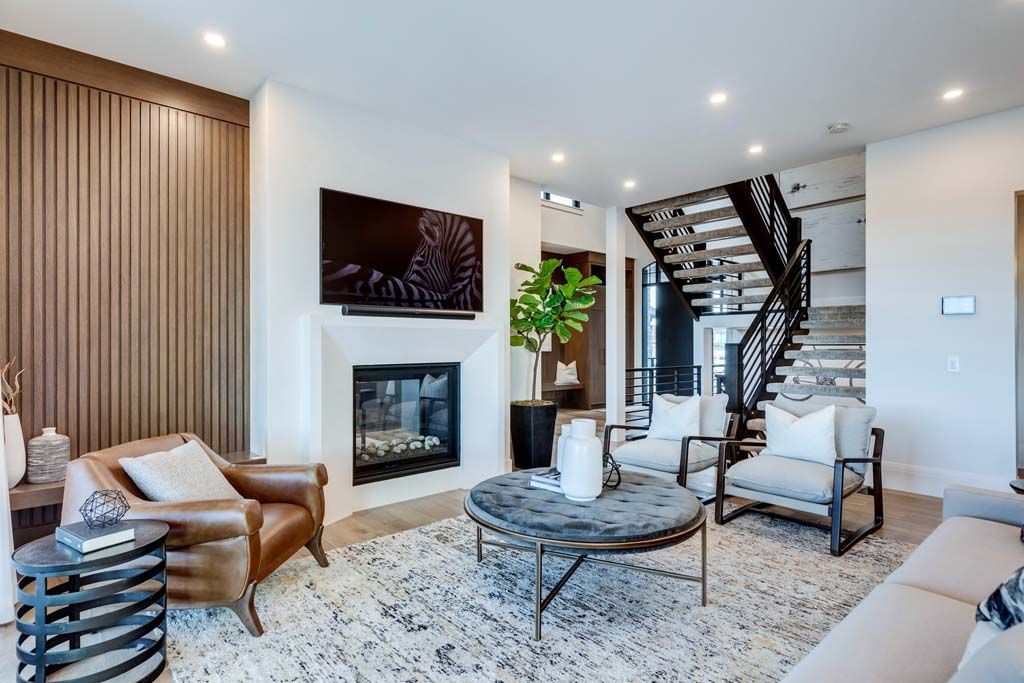 Living room with fireplace, TV, seating, and a staircase. Neutral colors with wood accents.