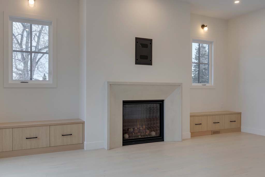 Bright, modern living room with fireplace between two windows, light wood cabinets below each window.
