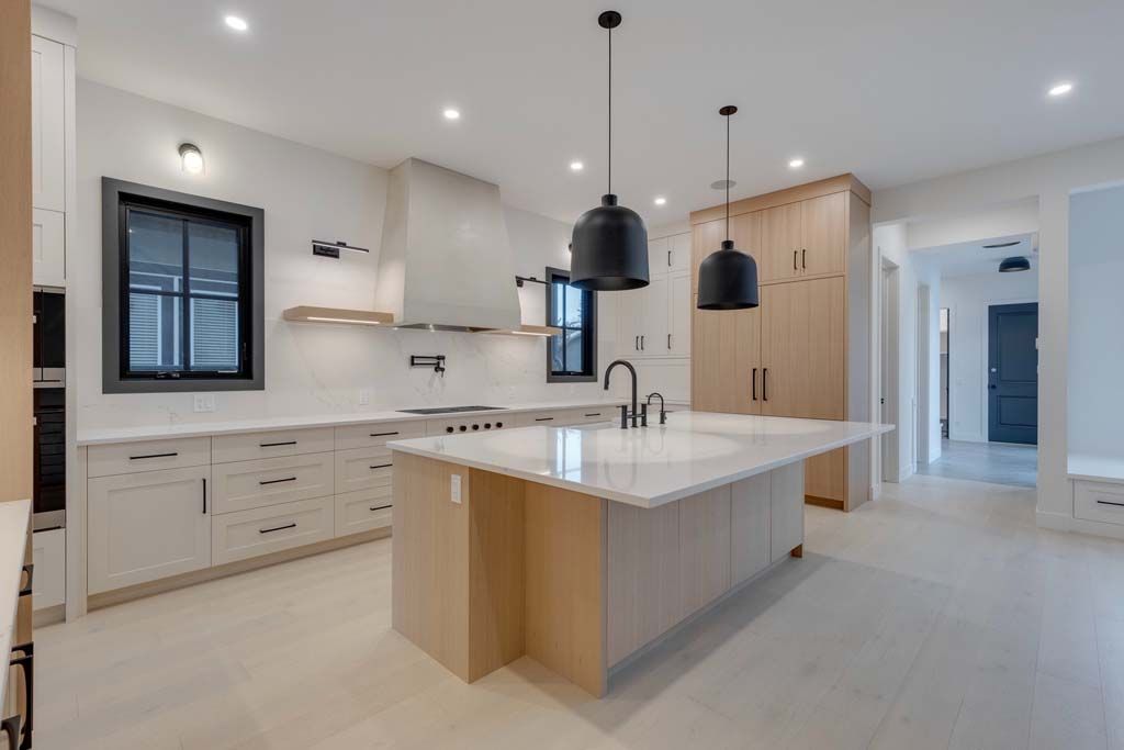 Modern kitchen with white countertops, light wood cabinetry, and black pendant lights.