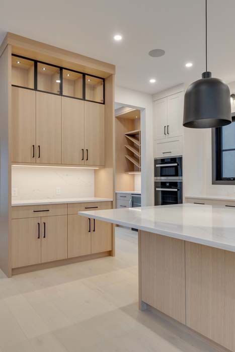 Modern kitchen with light wood cabinets, white countertops, and black accents.