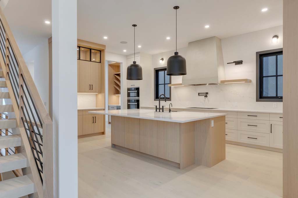 Modern kitchen with light wood cabinets, large island, black pendant lights, and stainless steel appliances.