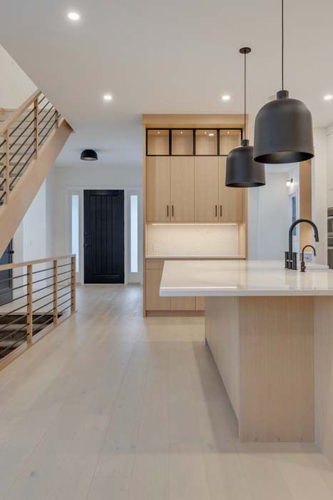 Modern kitchen with light wood cabinets, white countertops, and black pendant lights.