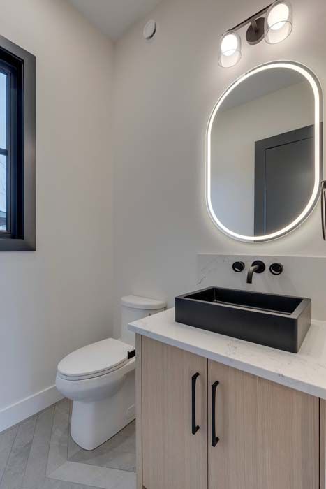 Modern bathroom with floating sink, black fixtures, oval mirror with light, and light wood cabinet.