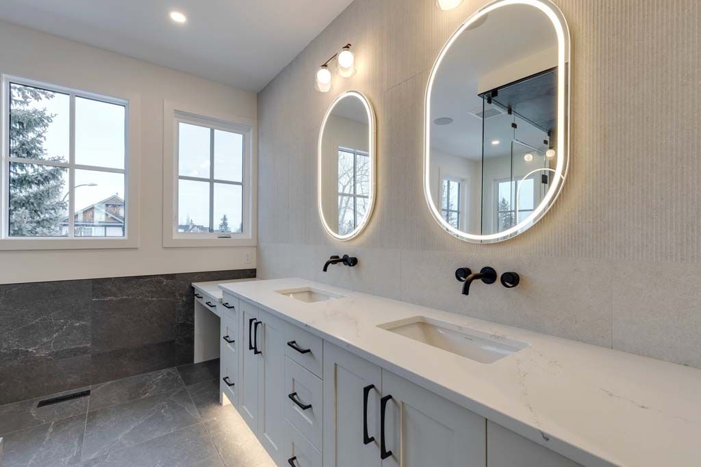 Modern bathroom with double vanity, oval backlit mirrors, and gray stone flooring.