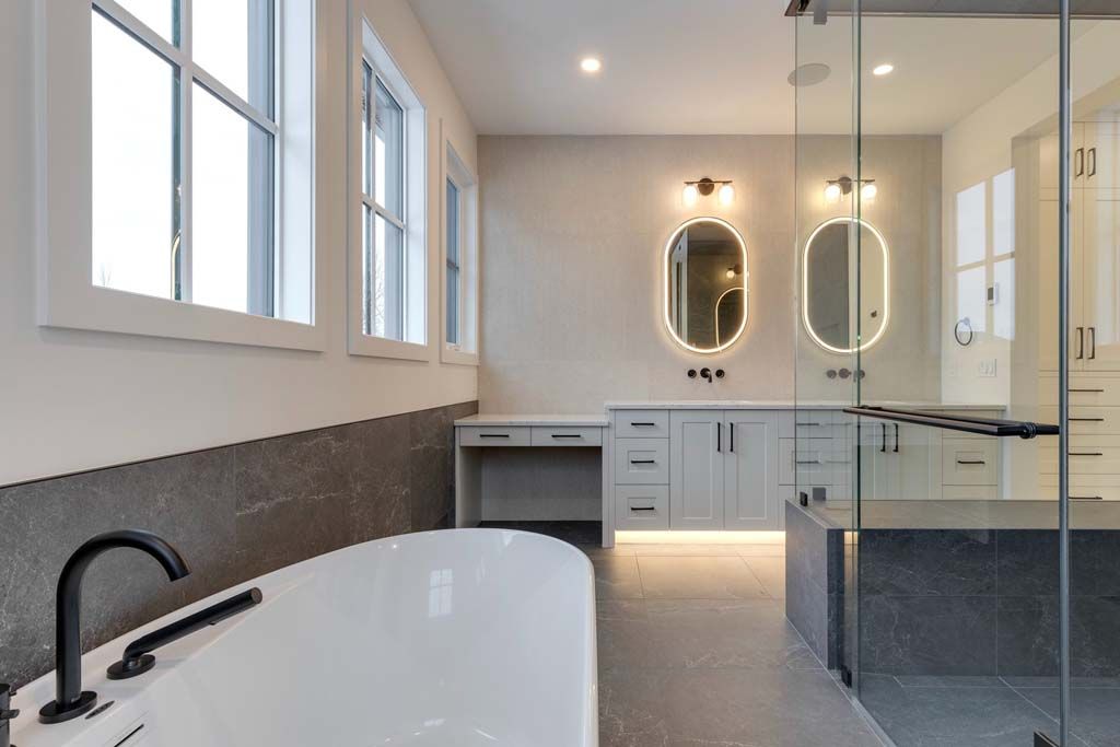 Modern bathroom with white tub, double vanity with oval mirrors, and glass shower.