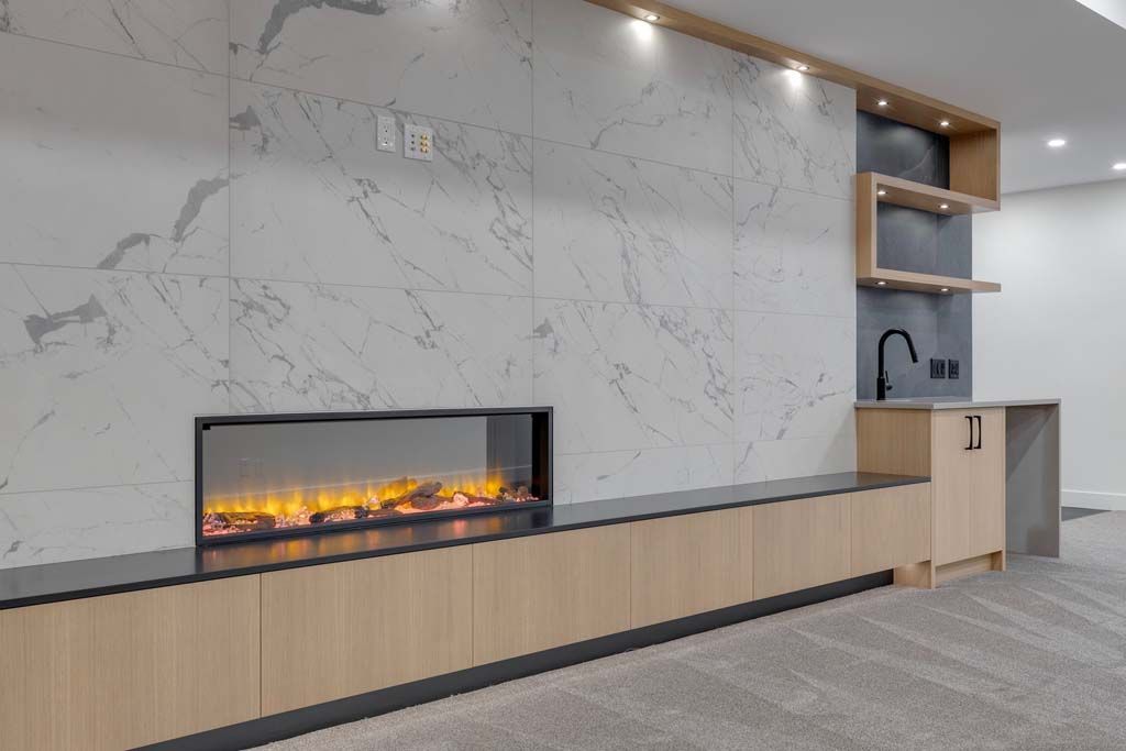Fireplace with a marble wall, wooden cabinets, and small bar in a room with a light carpet.