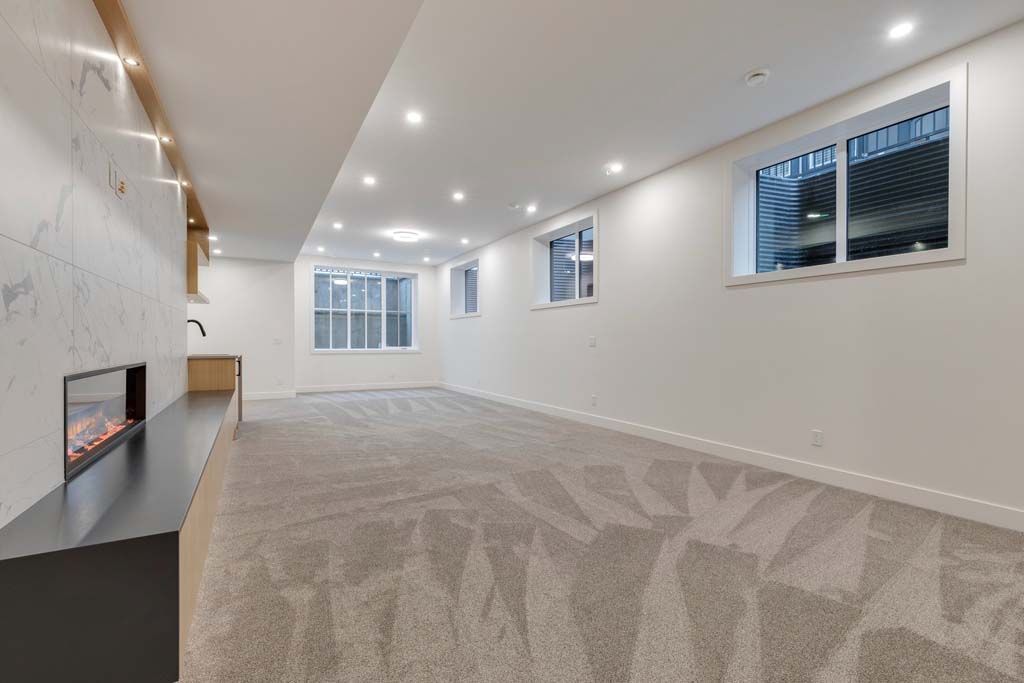 Empty, newly finished basement with light gray carpet, white walls, and fireplace.