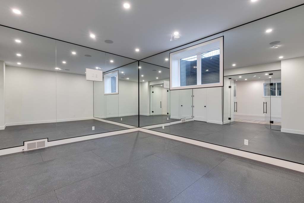 Gym with mirrors, rubber floor, and recessed lighting. Windows on one wall.
