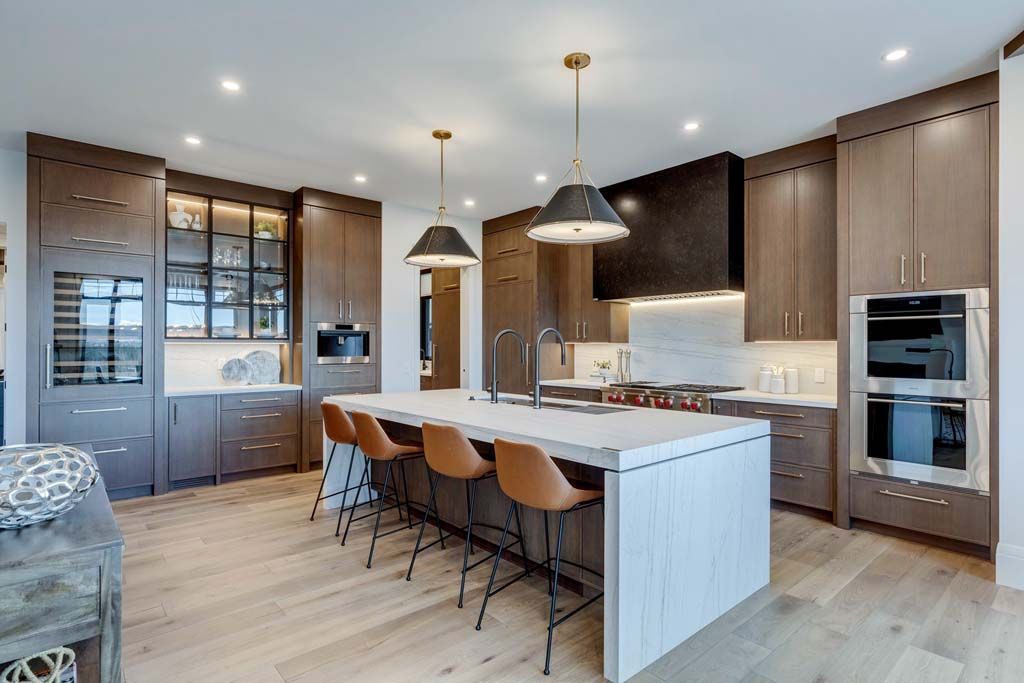 Modern kitchen with wooden cabinetry, island with seating, pendant lights, and stainless steel appliances.