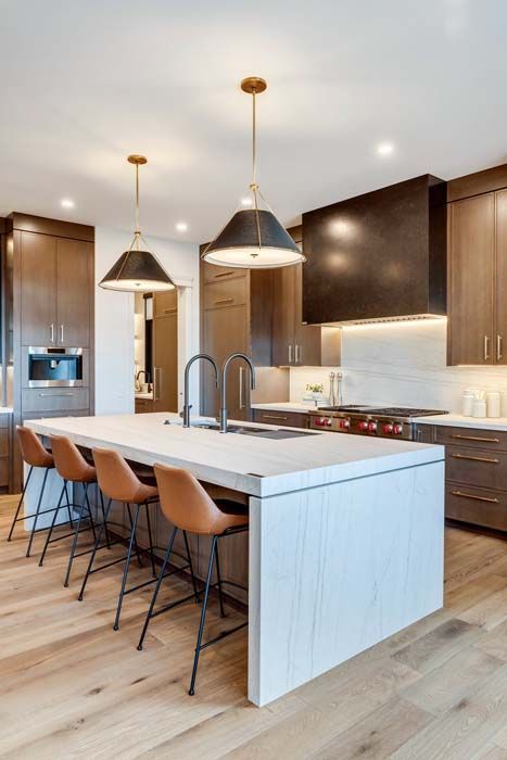 Modern kitchen with light wood flooring, an island with bar stools, and dark pendant lights.