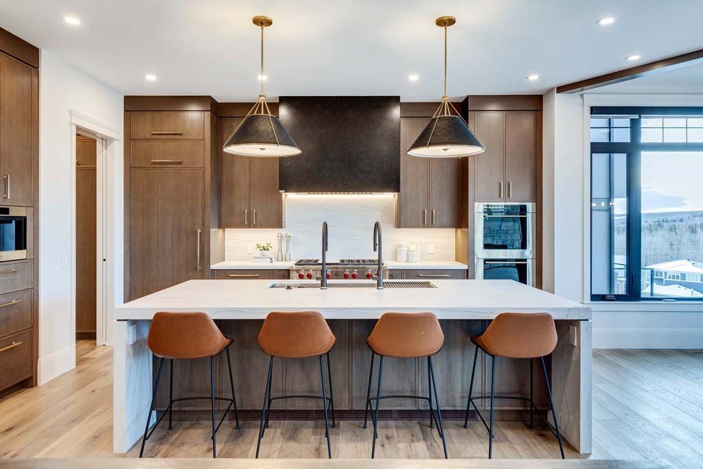 Modern kitchen with island, brown cabinets, pendant lights, and brown leather bar stools.