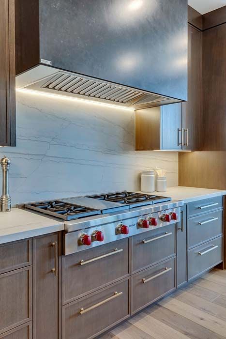 Modern kitchen with stainless steel range hood, stove, and light-colored countertops and cabinets.