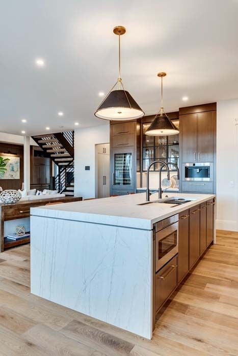 Modern kitchen with island, pendant lights, wooden cabinets, and stainless steel appliances.