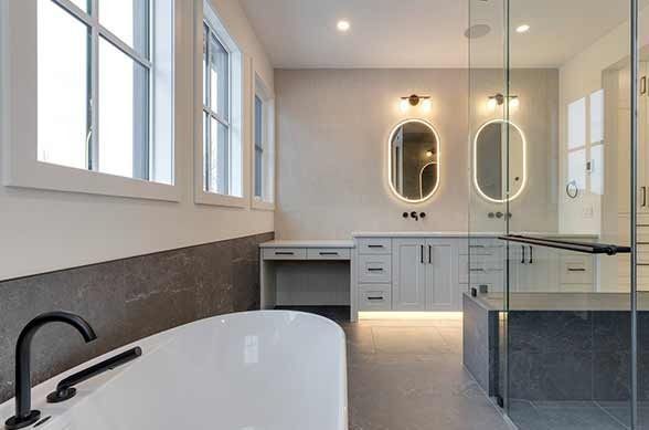 Modern bathroom with a bathtub, vanity with oval mirrors, and a glass shower.