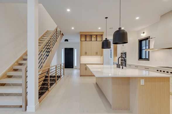 Modern kitchen and stairway with light wood accents and black pendant lights.