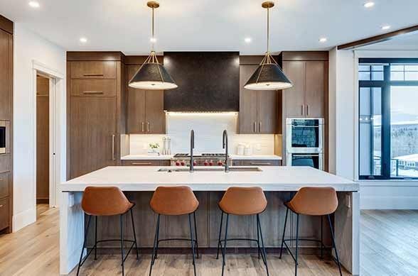 Modern kitchen with brown cabinets, white island, and copper pendant lights. Four brown bar stools.