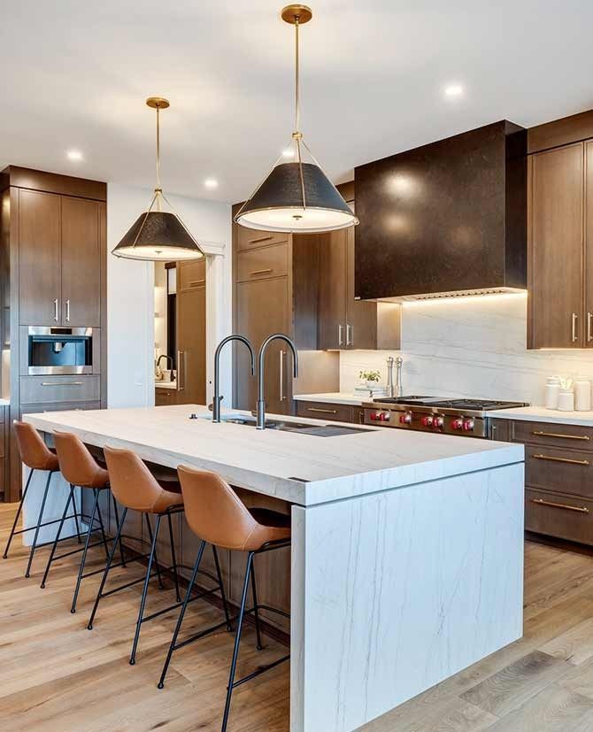 Modern kitchen with light wood floor, island with bar stools, brown cabinets, and overhead pendant lights.