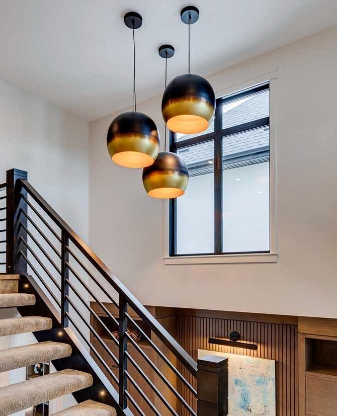 Staircase with three black and gold pendant lights hanging near a window, brown wainscoting.