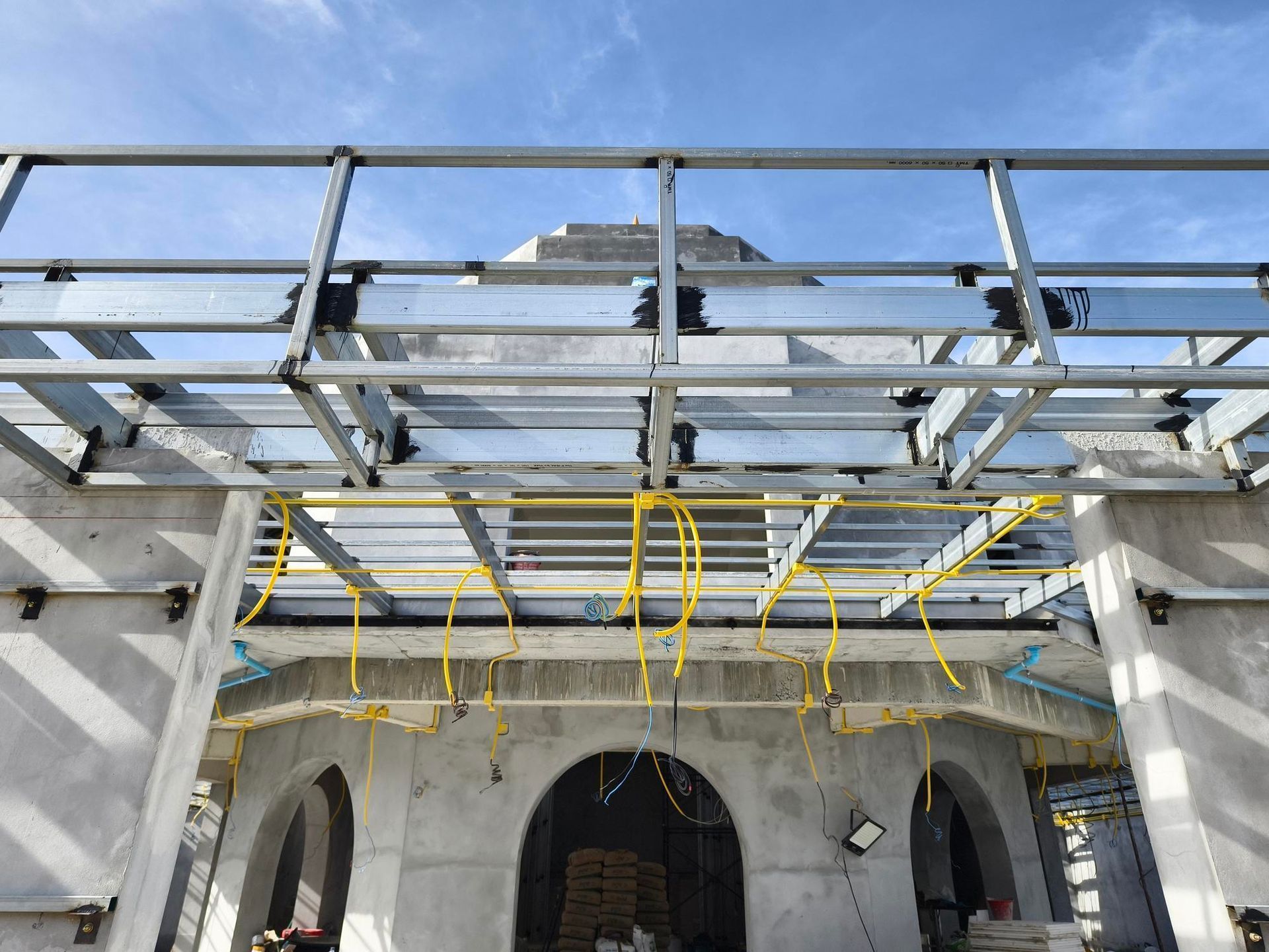 Construction of a building's facade, showing a metal frame ceiling with electrical wiring against a blue sky.