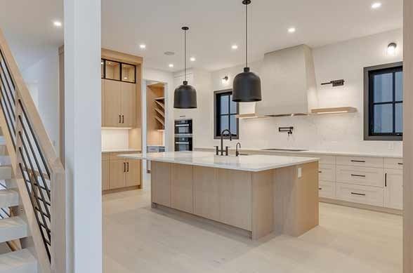 Modern kitchen with light wood cabinetry, white countertops, black pendant lights, and island.