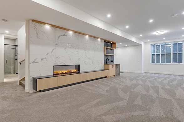 Empty basement room with fireplace, built-in cabinets, marble wall, and large window.