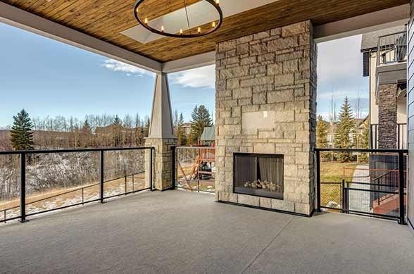 Outdoor patio with a stone fireplace, glass railing, and a view of trees and sky.
