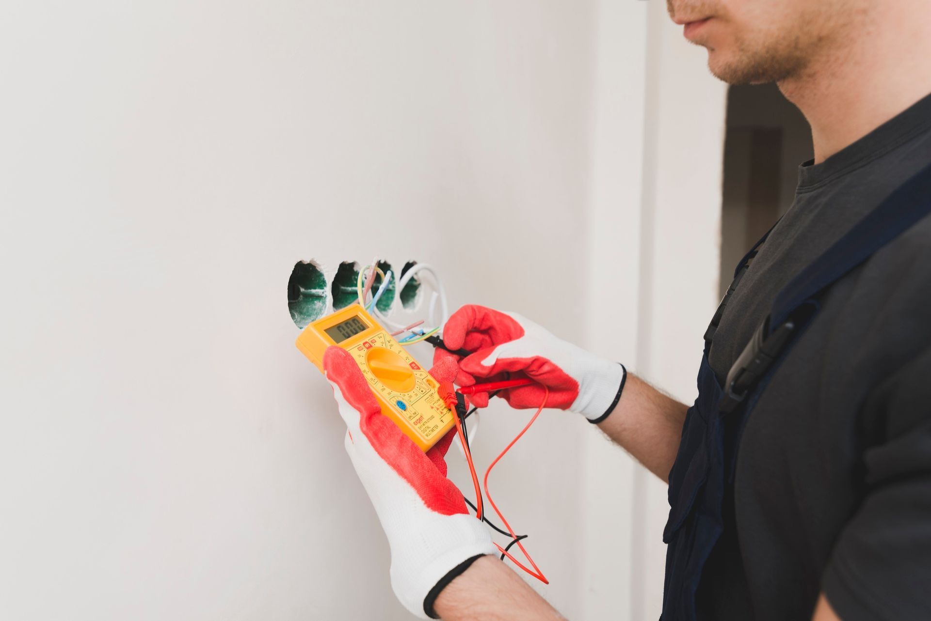 An electrician using a multimeter on a wall outlet.