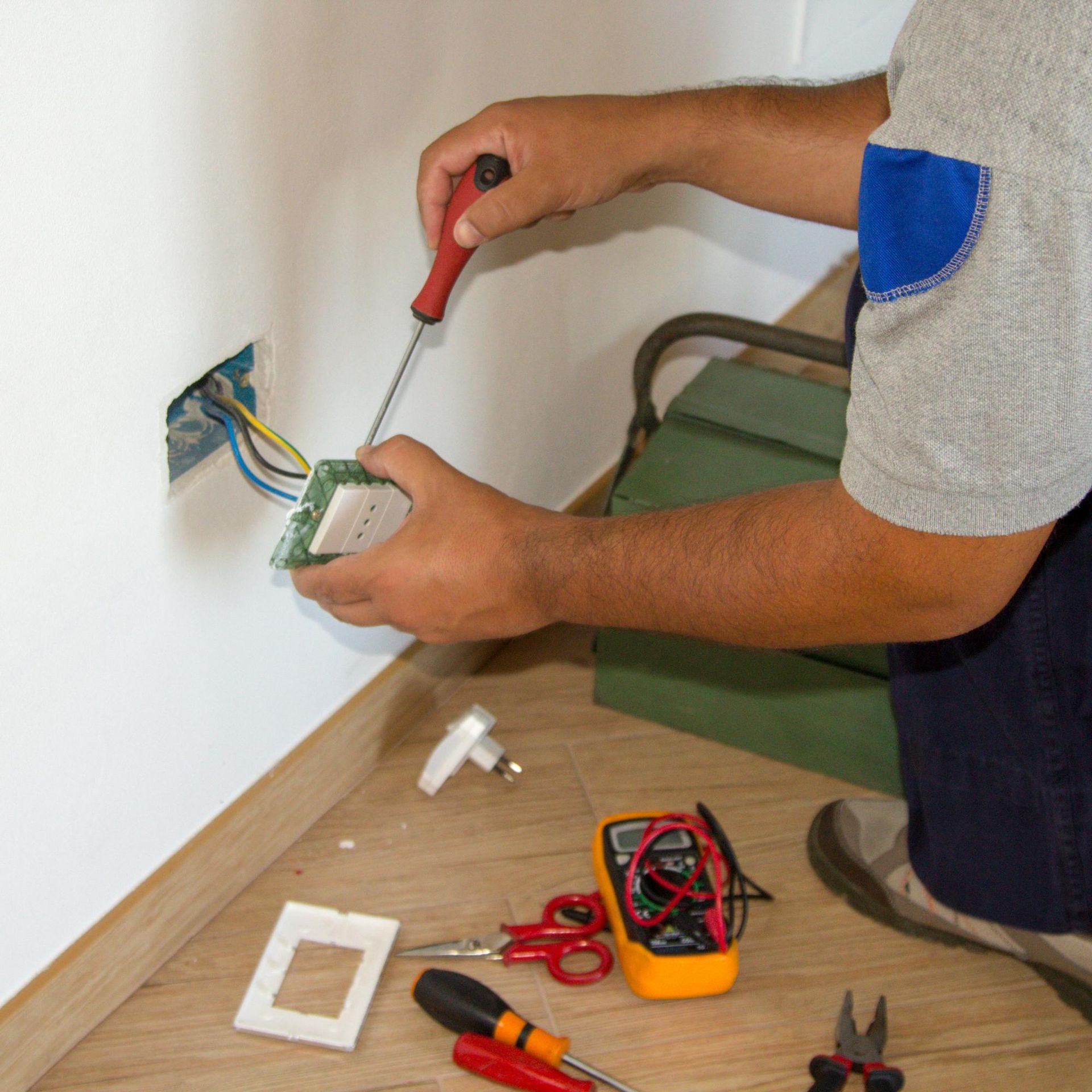 Electrician repairing an electrical outlet, using a screwdriver, indoors.