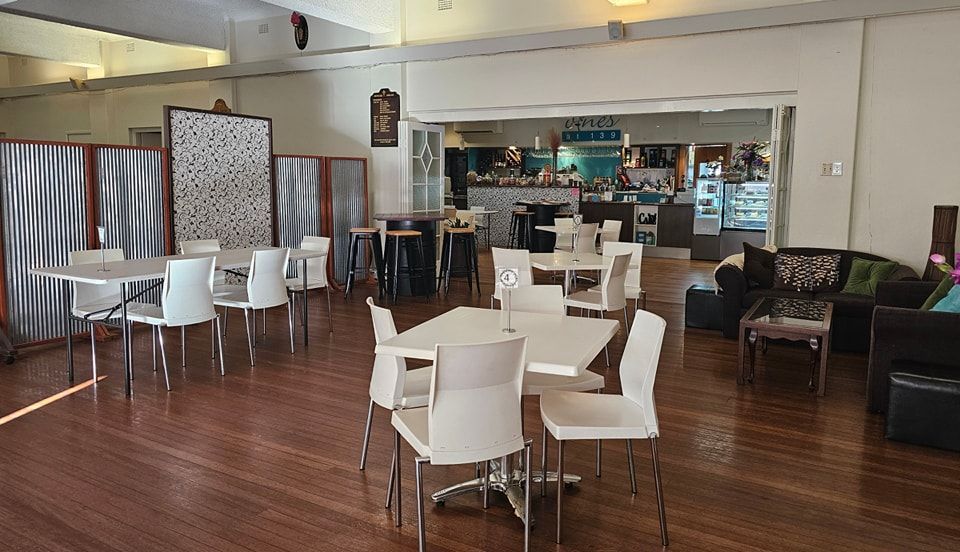Long white dining table set for guests with white chairs, artwork, and plants — Vines at 139 in Grafton, NSW