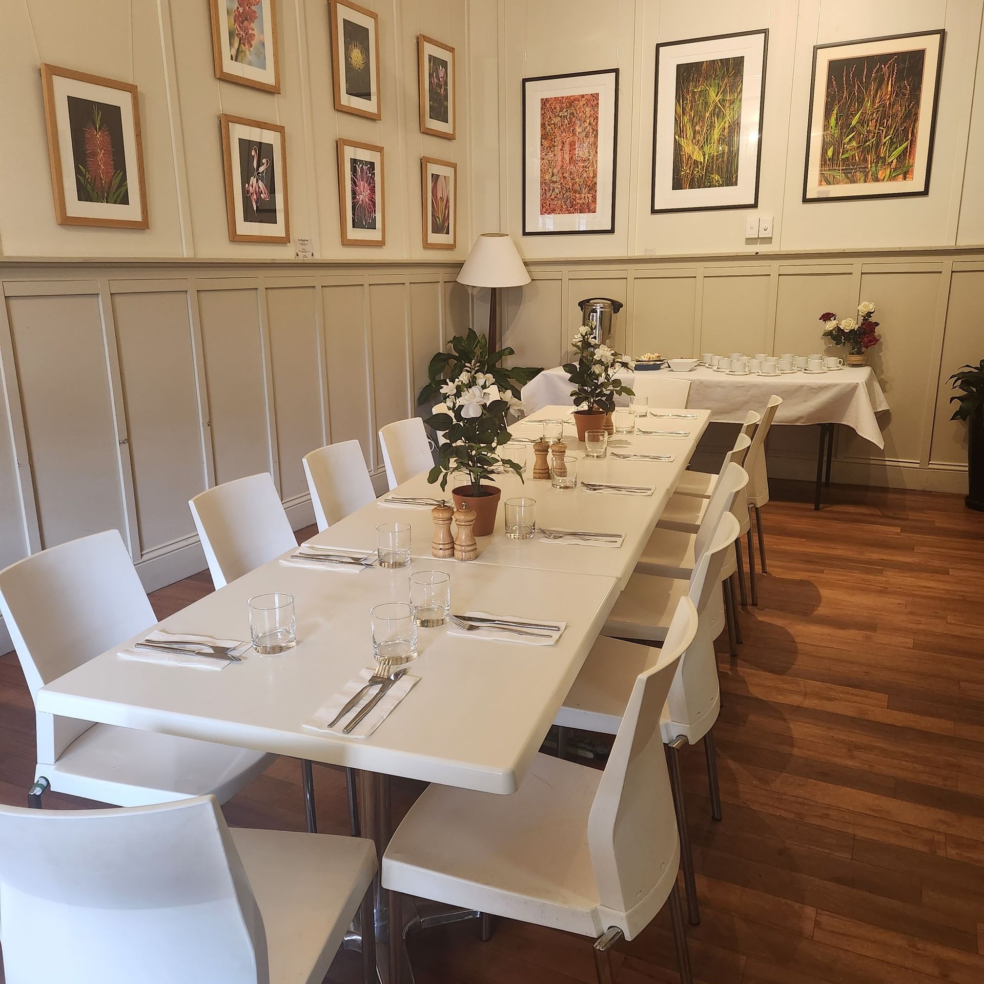 A long white dining table set for a meal, with chairs, plants, and art on the walls.