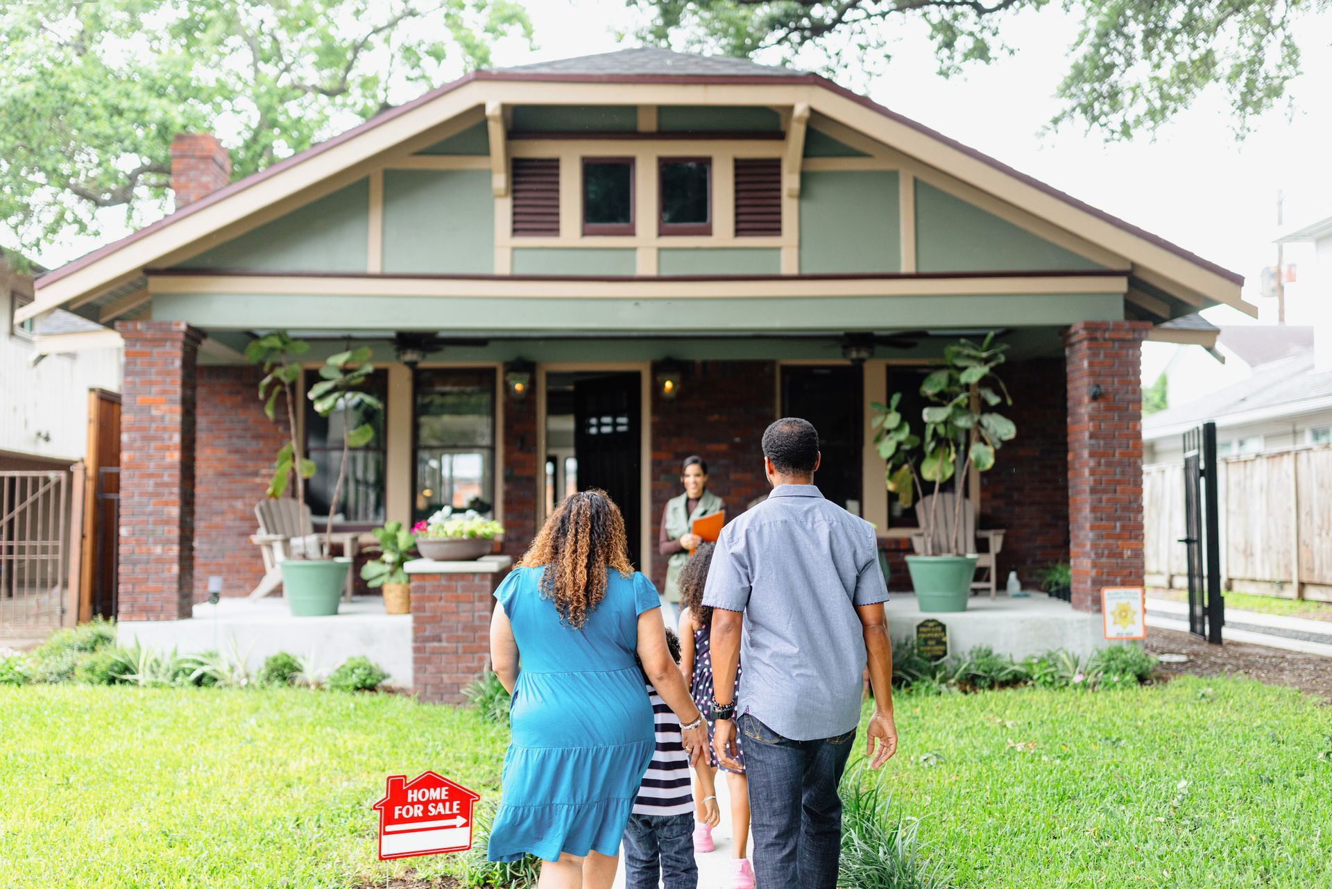 A family is walking towards a house with a for sale sign in front of it.