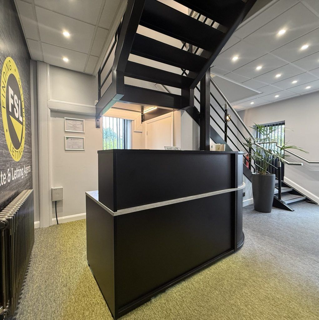 Modern office lobby with a black reception desk, staircase, and gray carpeted floor