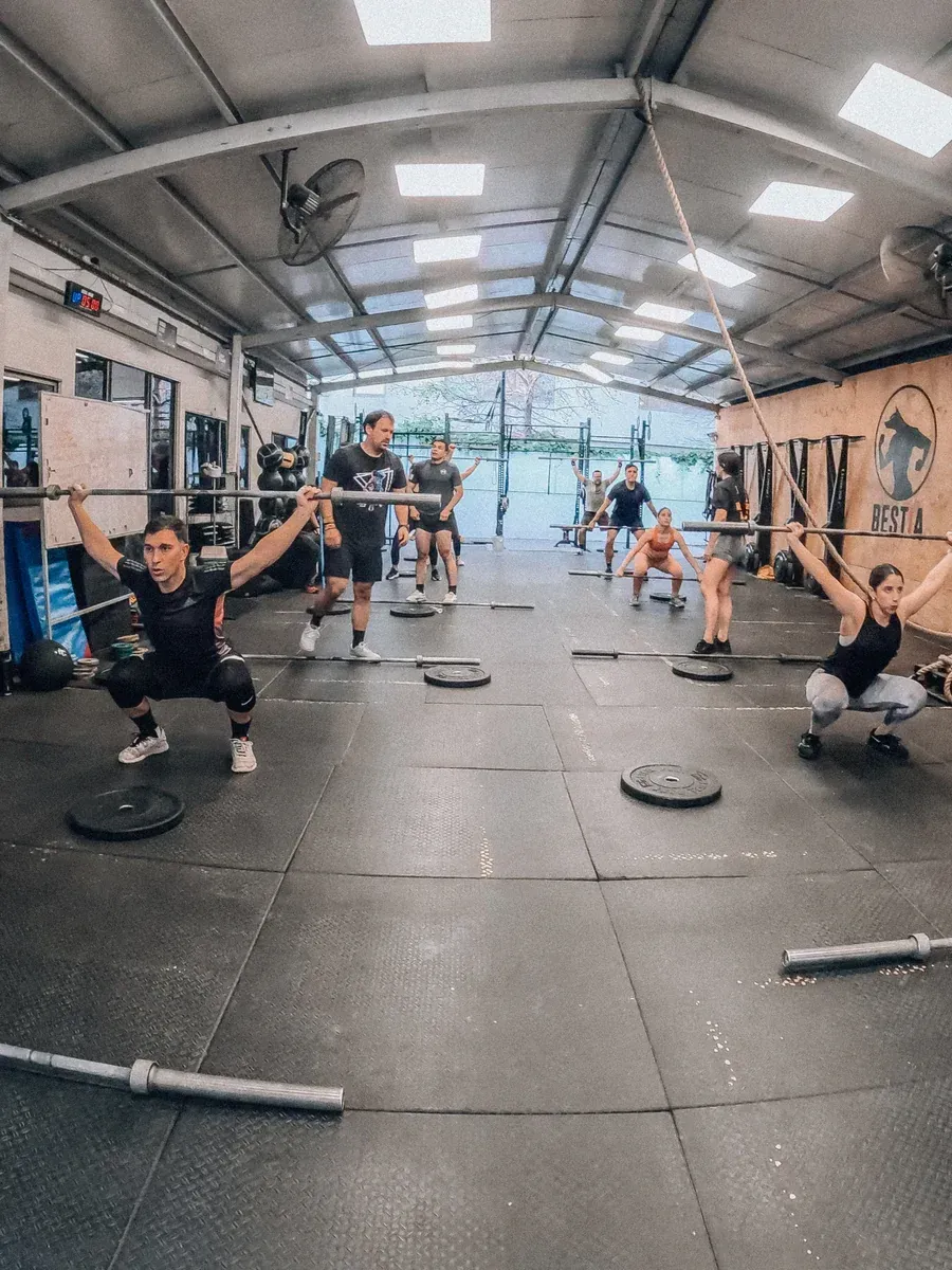 Personas en un gimnasio realizando ejercicios de levantamiento de pesas con barras.
