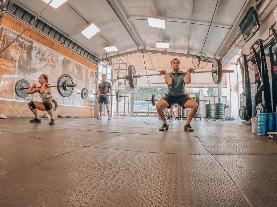 Personas en un gimnasio realizando ejercicios de levantamiento de pesas con barras.
