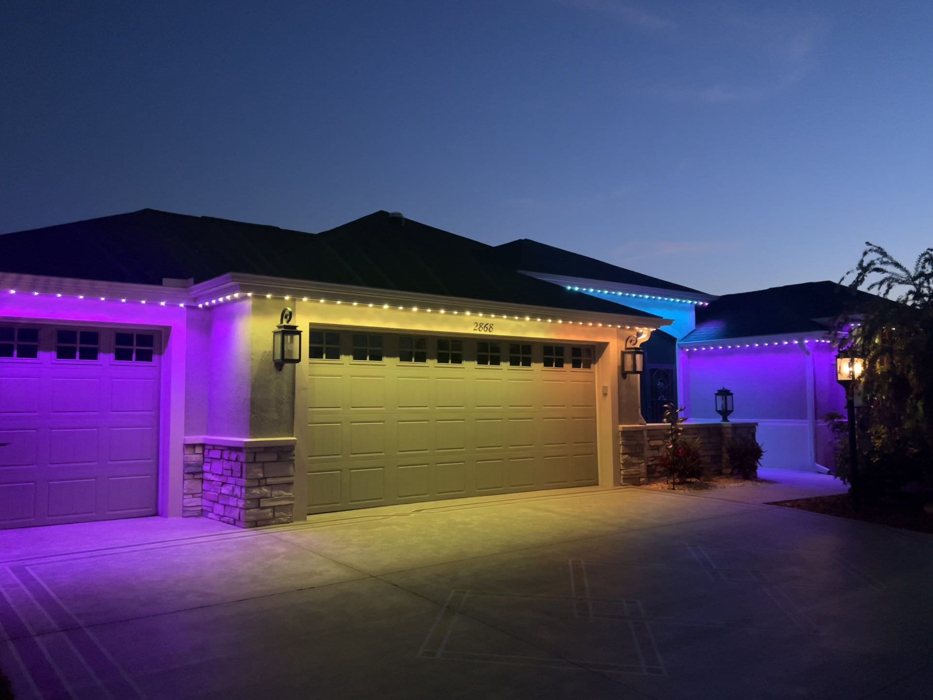 Suburban house garage lit with purple and yellow holiday lights at night