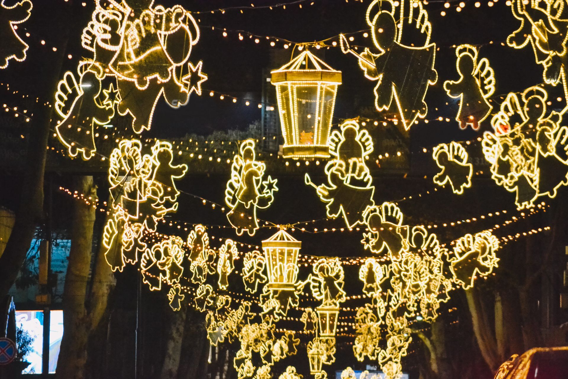 Glowing lanterns and string lights hang over a street at night, forming festive animal shapes and a central lantern