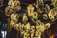 Glowing lanterns and string lights hang over a street at night, forming festive animal shapes and a central lantern