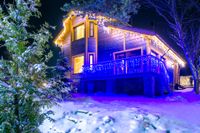 Snowy cabin at night glowing with blue and warm lights under trees