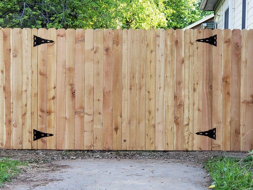 A wooden fence with black hinges is sitting next to a driveway.
