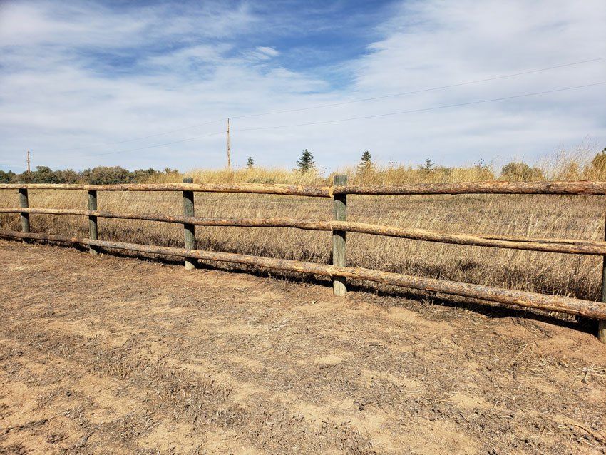 A wooden fence is in the middle of a dirt field.