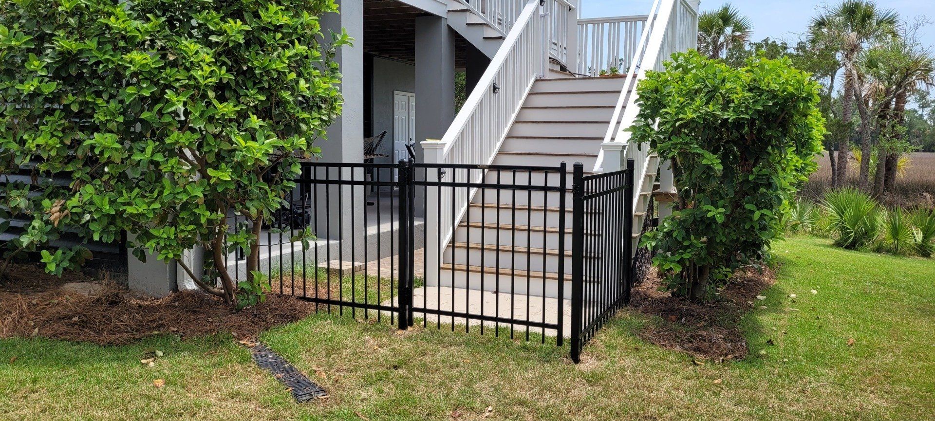 A black fence is in front of a house with stairs leading up to it.