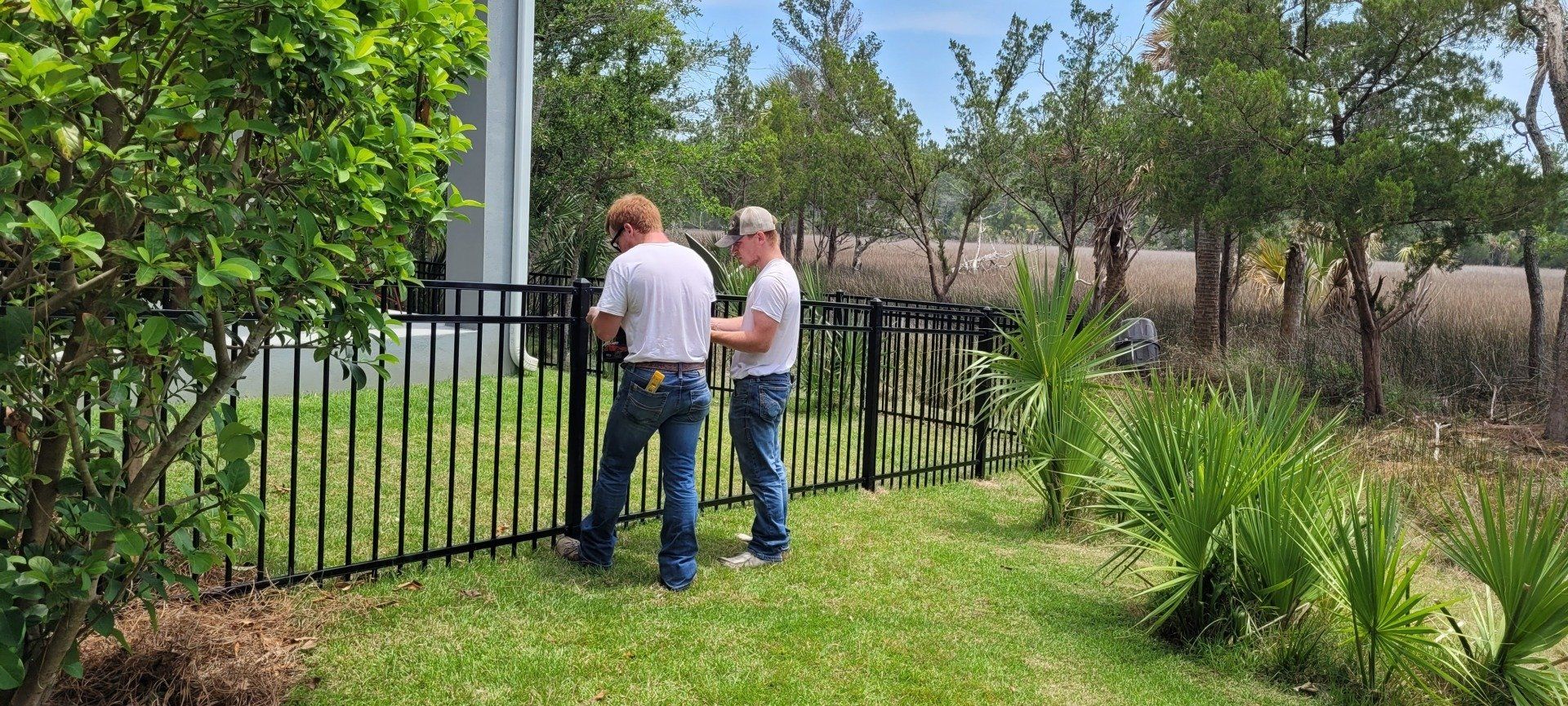 Two men are working on a metal fence in a yard.