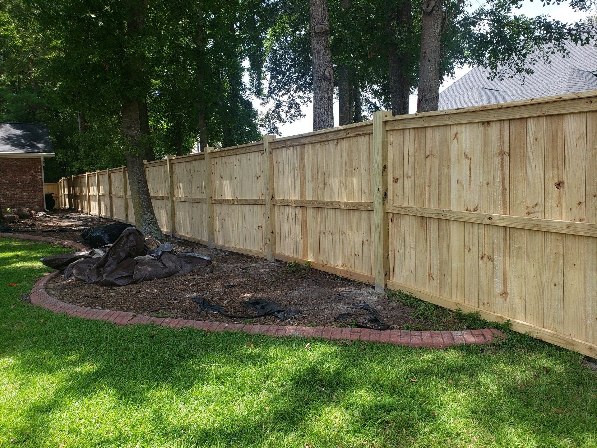 A wooden fence is in the middle of a lush green yard.