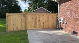 A wooden fence is surrounding a driveway in front of a brick house.