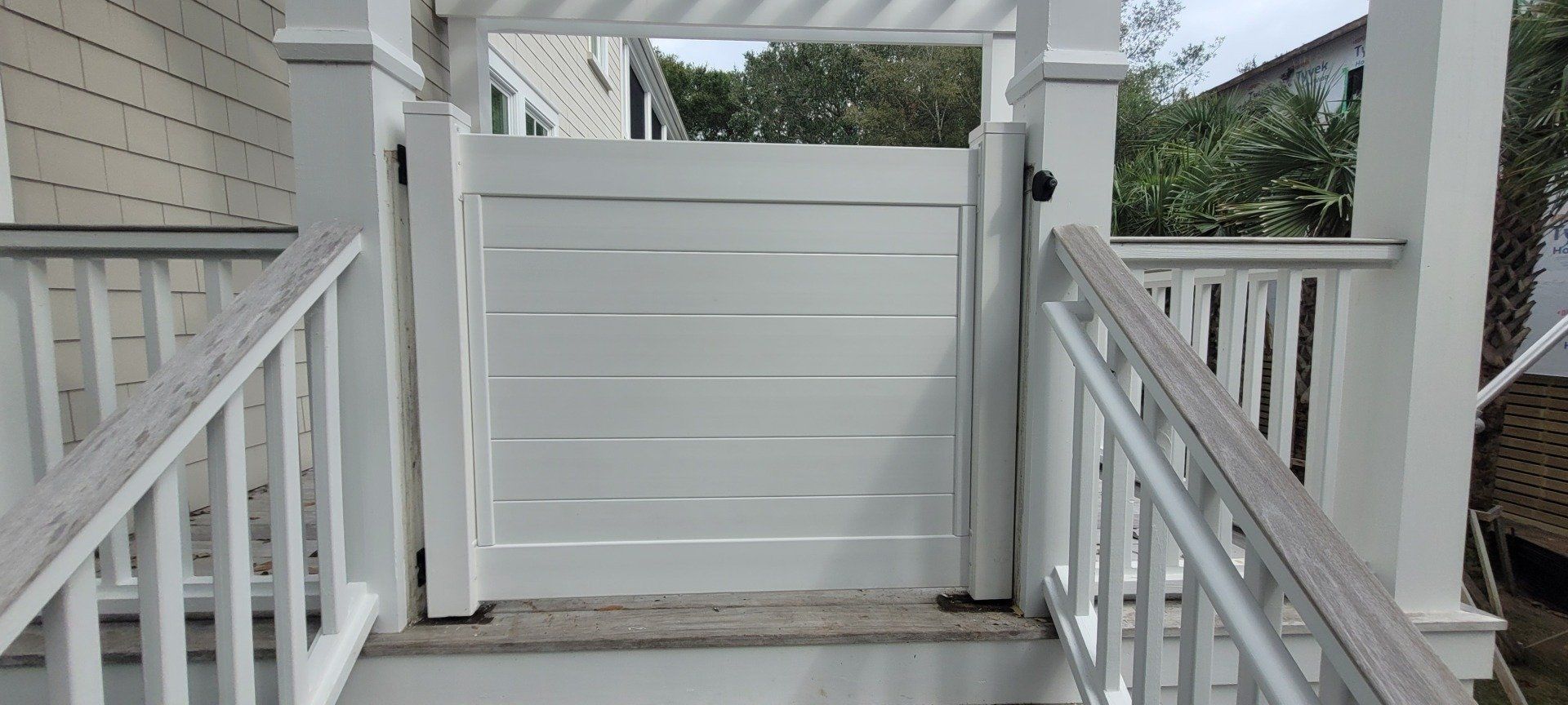 A white gate is leading to a porch with stairs.