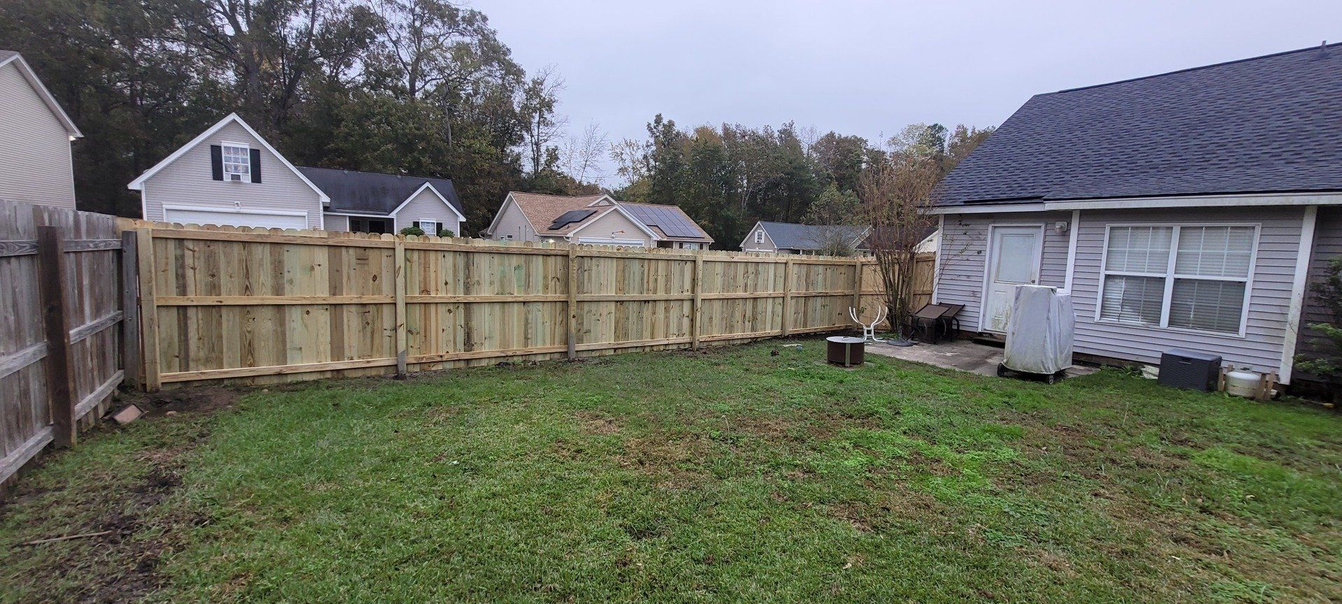 A backyard with a wooden fence and a house in the background.