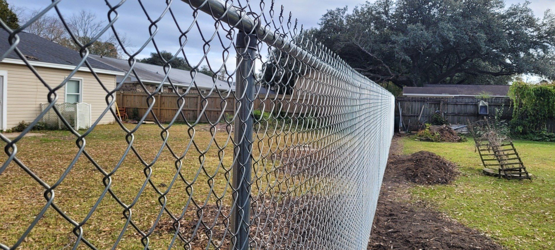 A chain link fence is broken in half in a backyard.