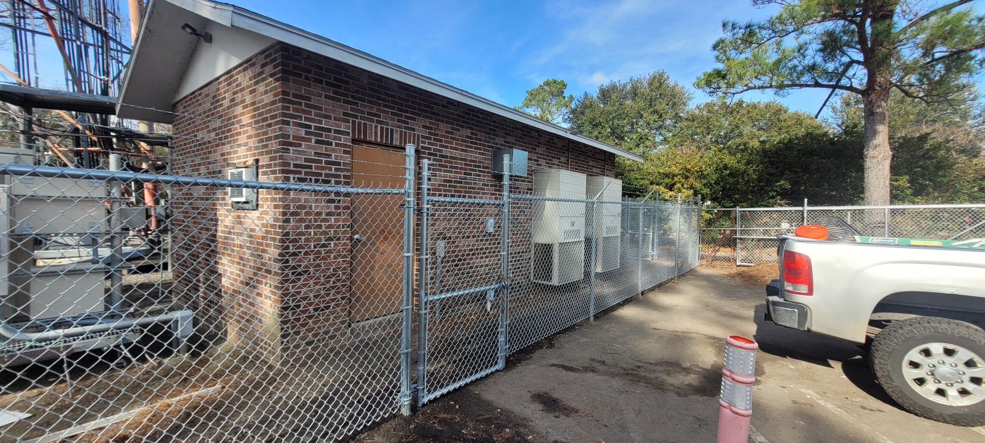 A white truck is parked in front of a brick building behind a chain link fence.