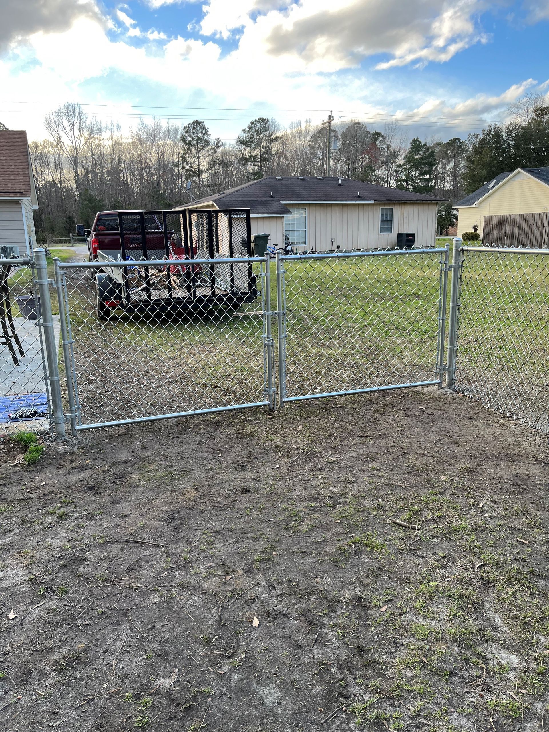 A chain link fence is sitting in the middle of a dirt field in front of a house.
